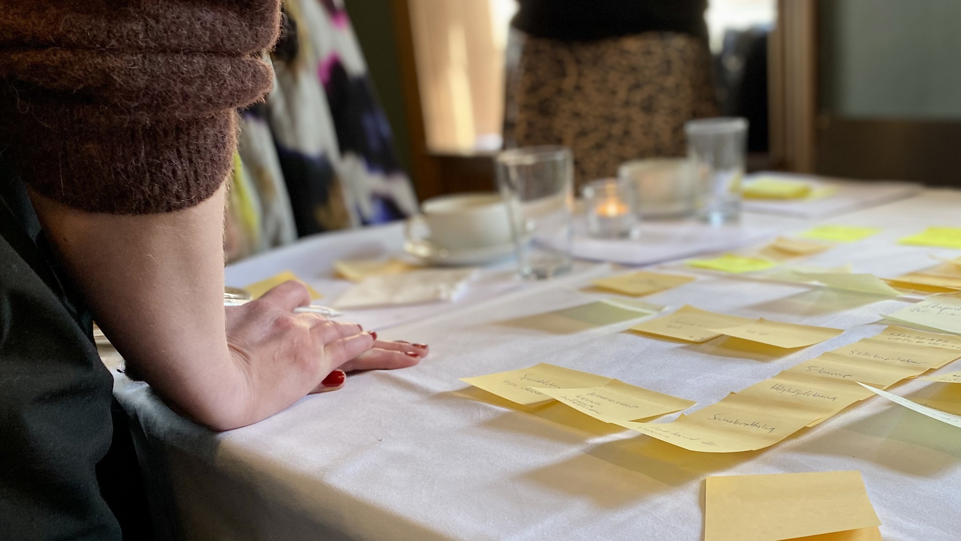 Post-it lappar på ett bort, en hand på bordet och fler personer syns stå runt borded.