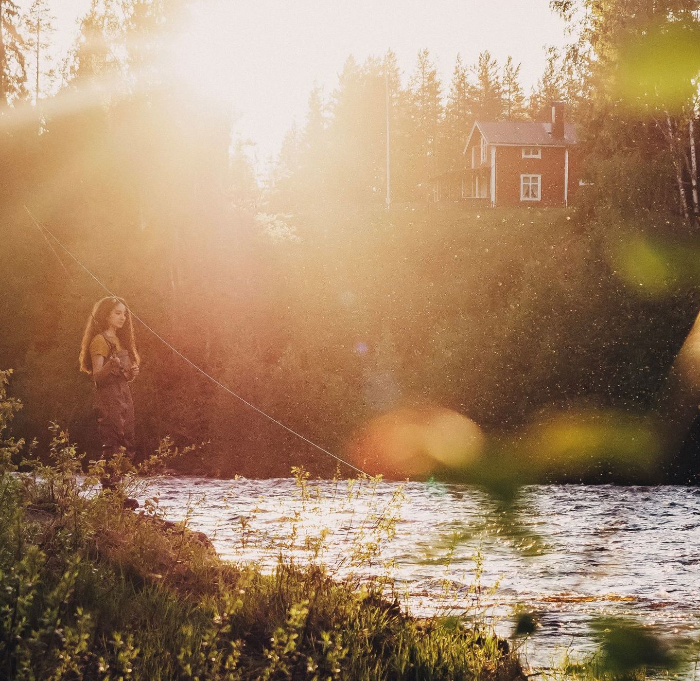 En kvinna fiskar vid en älv i solnedgång.