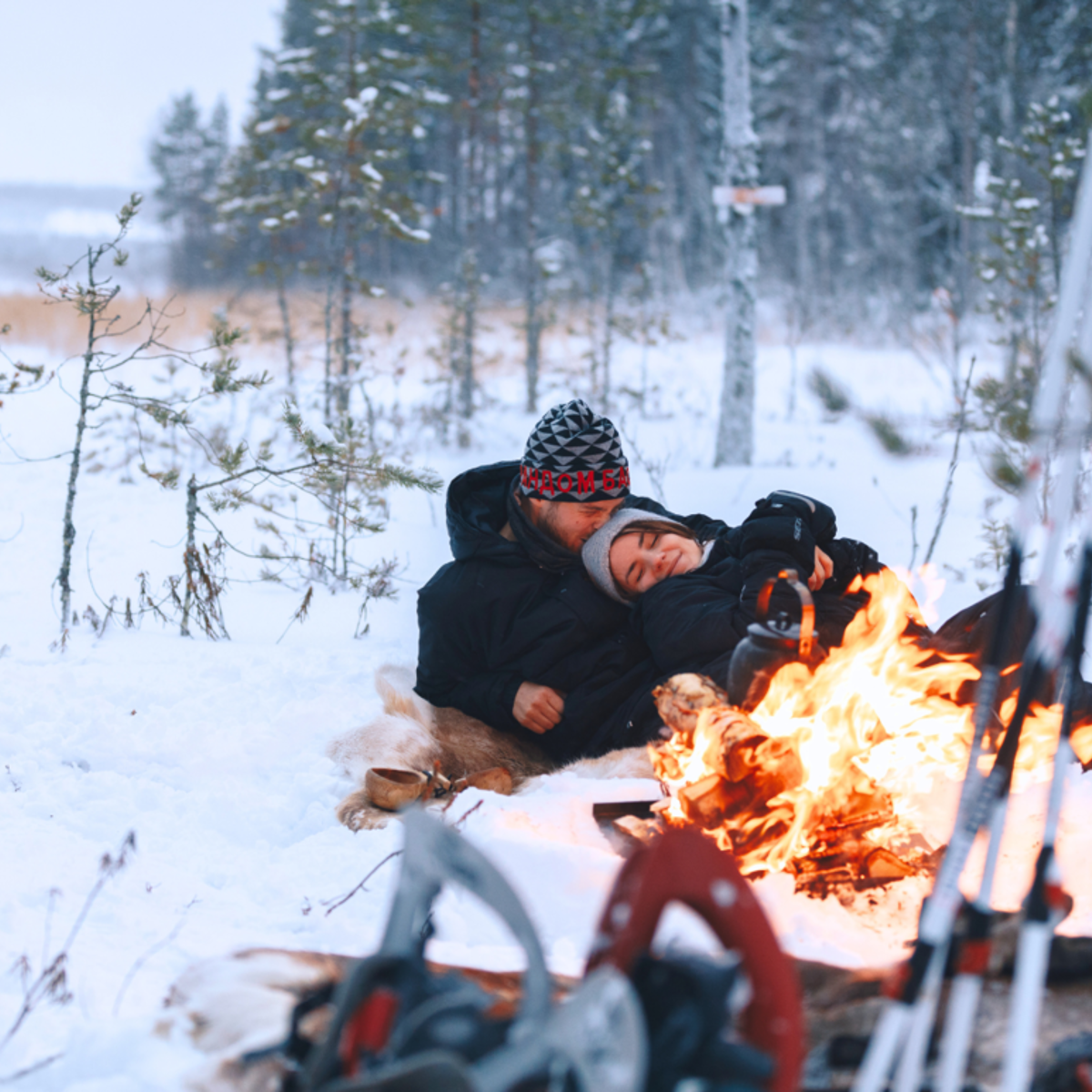 A man and a women by a campfire in the forest. 
